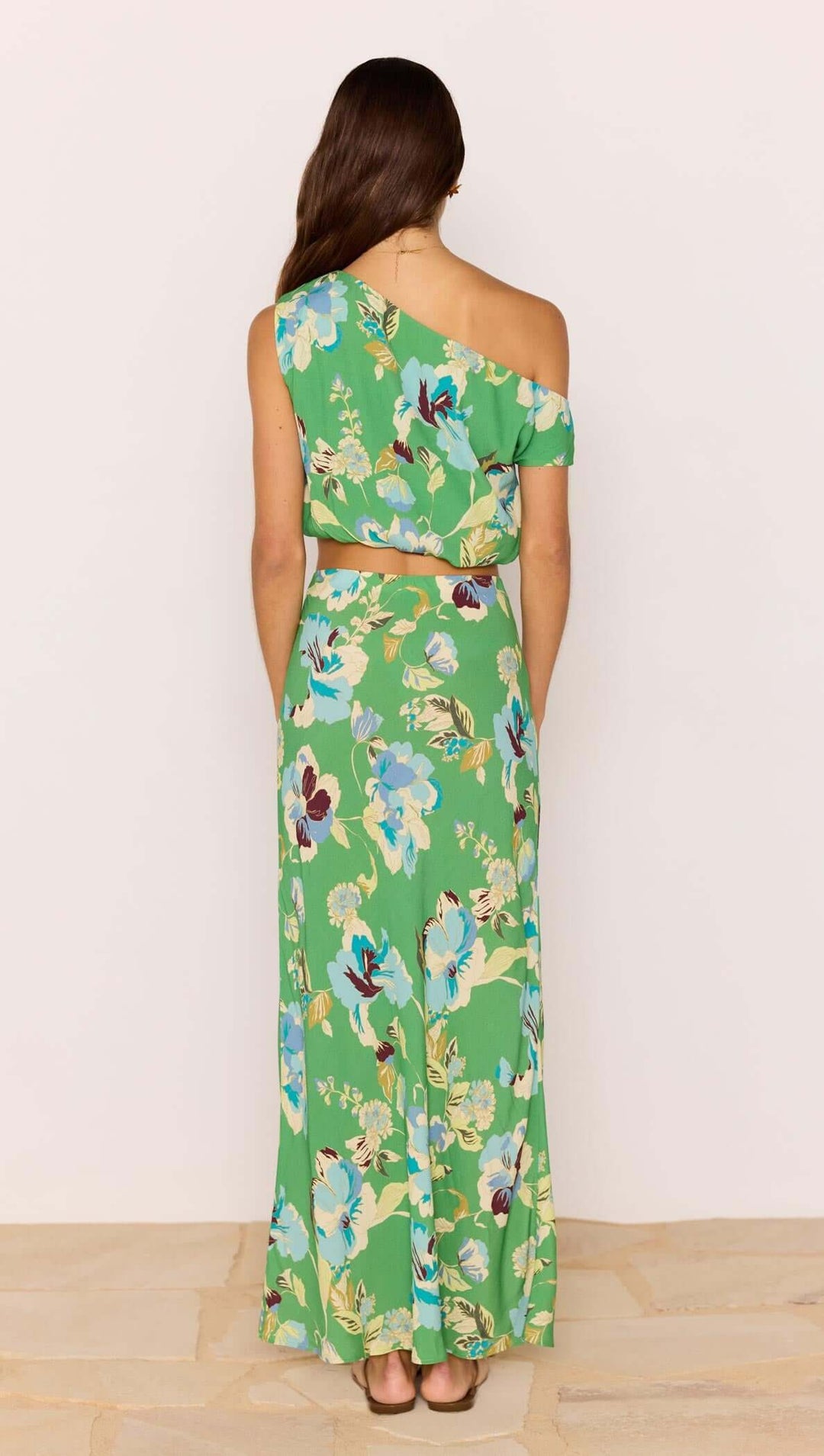 Woman wearing a green floral one-shoulder dress against a white background