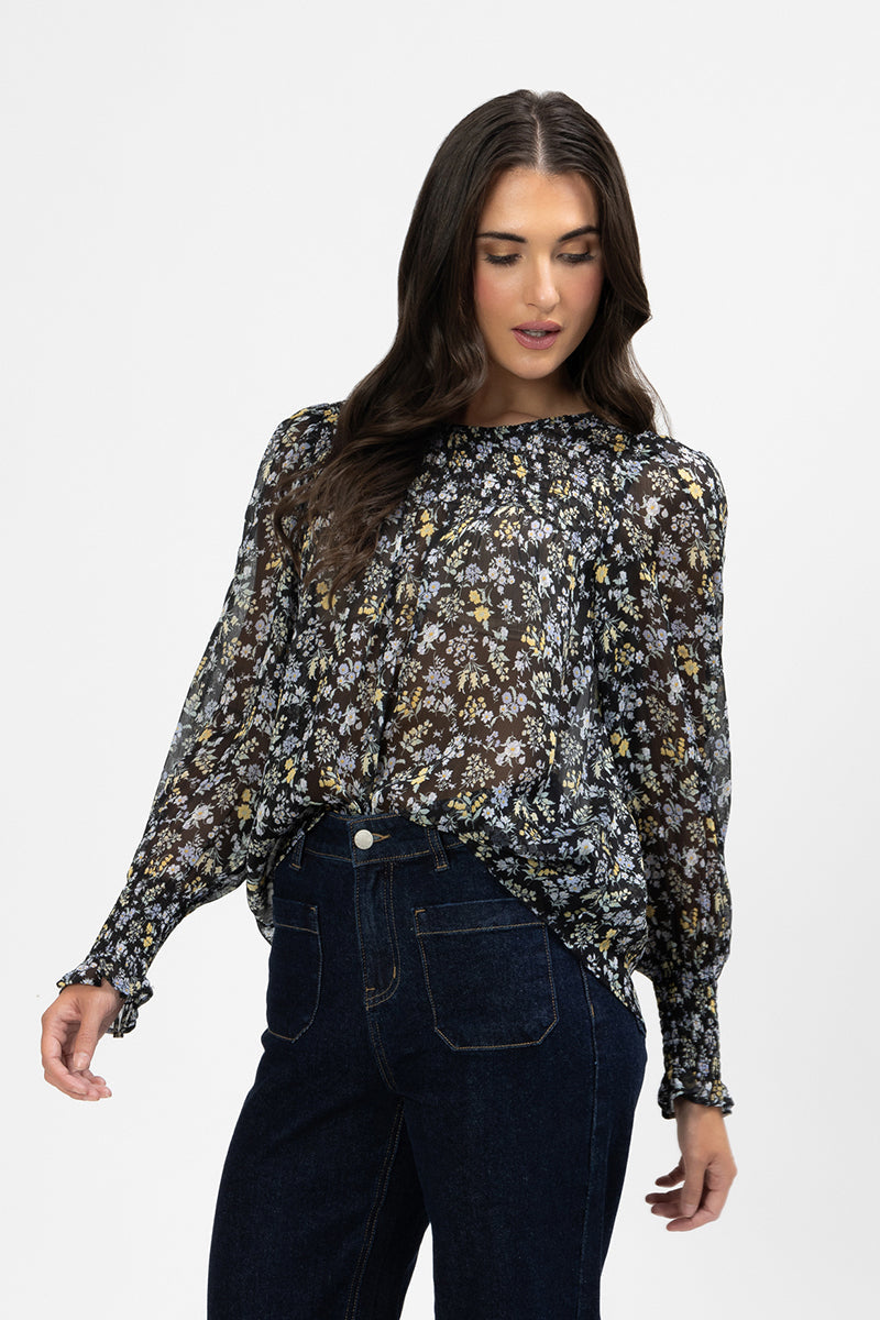 Woman wearing a floral hug me blouse and dark jeans on a white background