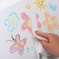 Hand using a towel to wipe over children's drawings of flowers and butterflies on a white surface.