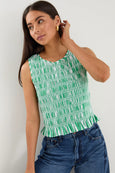 Woman wearing a green and white patterned sleeveless top with blue jeans against a plain background