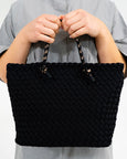 Black woven handbag held by a person against a neutral background