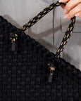 Black woven handbag with decorative handle against a neutral background