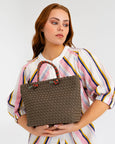 Woman holding a woven brown handbag against a plain background
