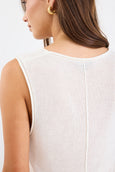 Close-up of a person wearing a white sleeveless top on a plain background