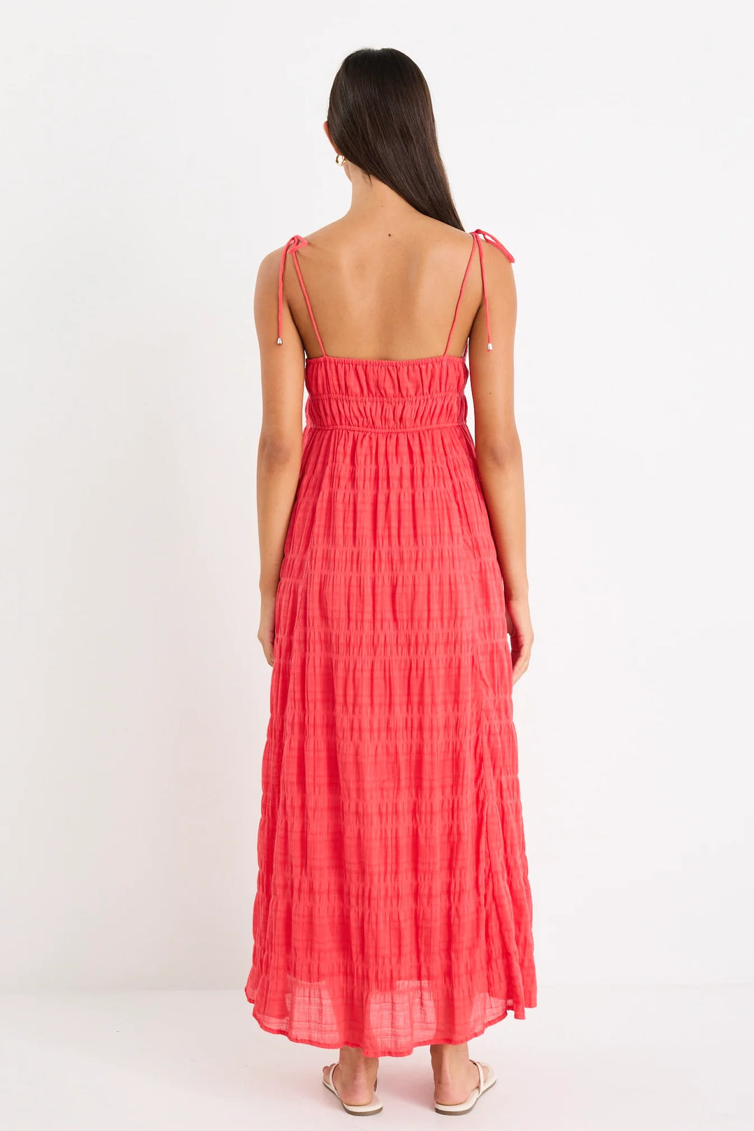 Woman wearing a coral pink dress with thin straps on a white background