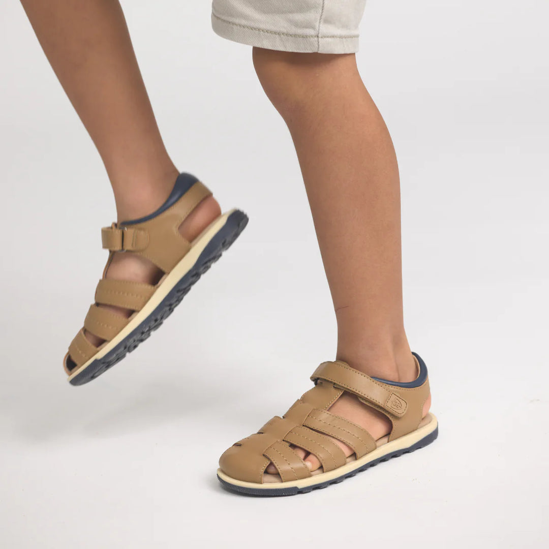 Tan sandals with blue soles worn by a person on a light gray background