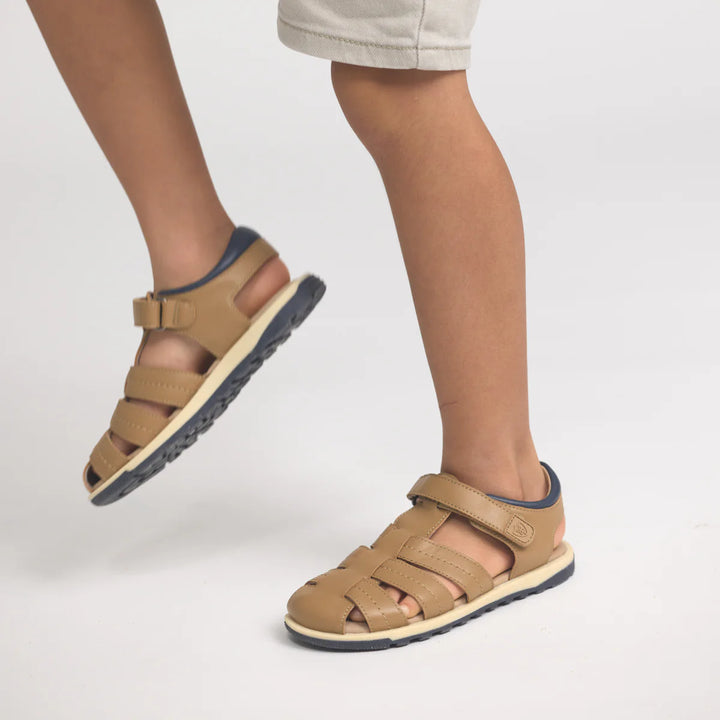 Tan sandals with blue soles worn by a person on a light gray background