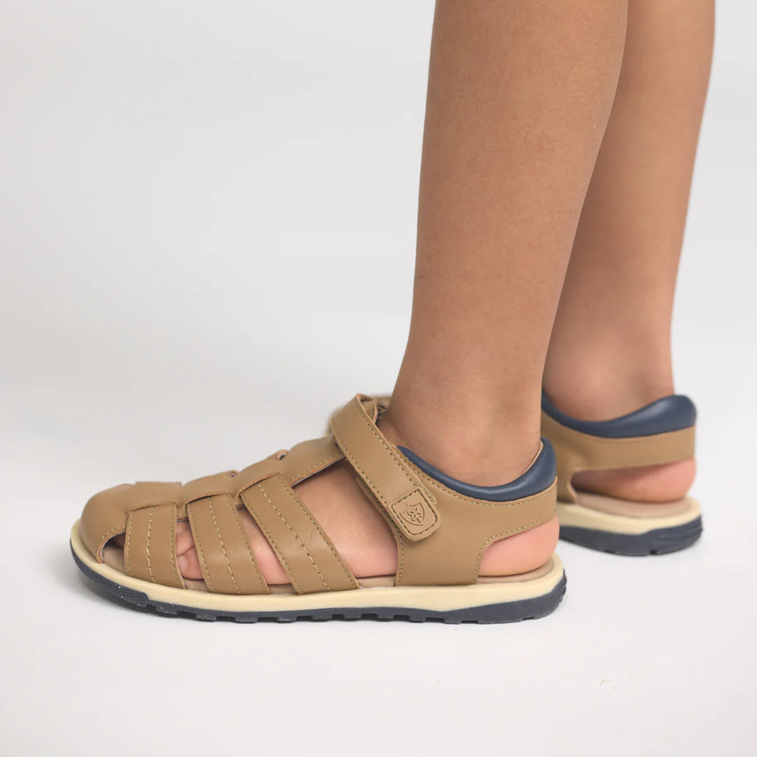 Children's feet wearing tan sandals with blue soles on a white background