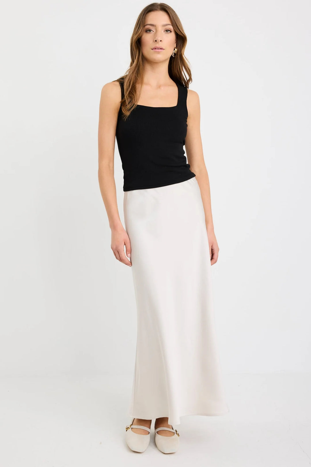 Woman wearing a black sleeveless top and white pants on a white background