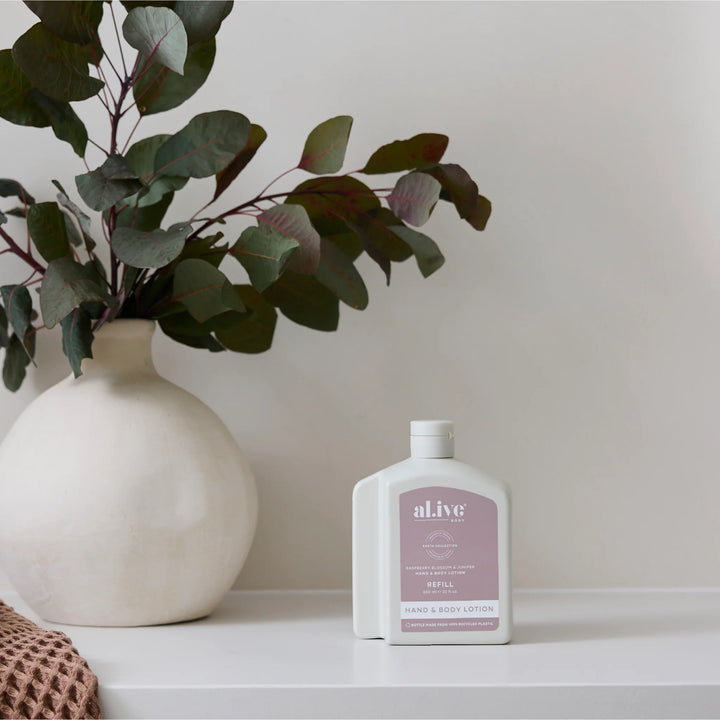 Lotion bottle labeled 'alive' next to a vase with greenery on a white surface.