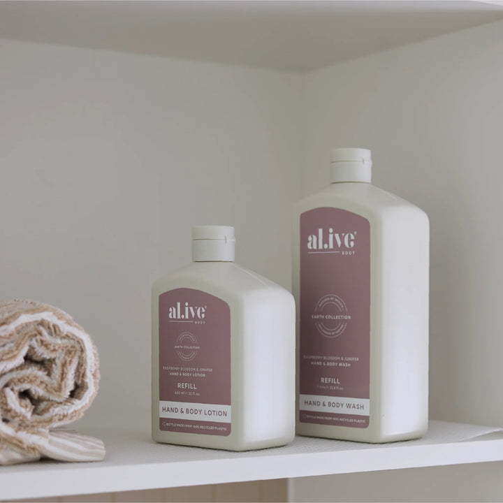 Two bottles of 'aLive' hand and body products on a shelf with a towel.