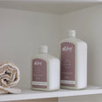 Two bottles of 'aLive' hand and body products on a shelf with a towel.