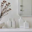 Bathroom setting with 'alive' skincare products on a shelf, a vase with dried flowers, and a mirror.