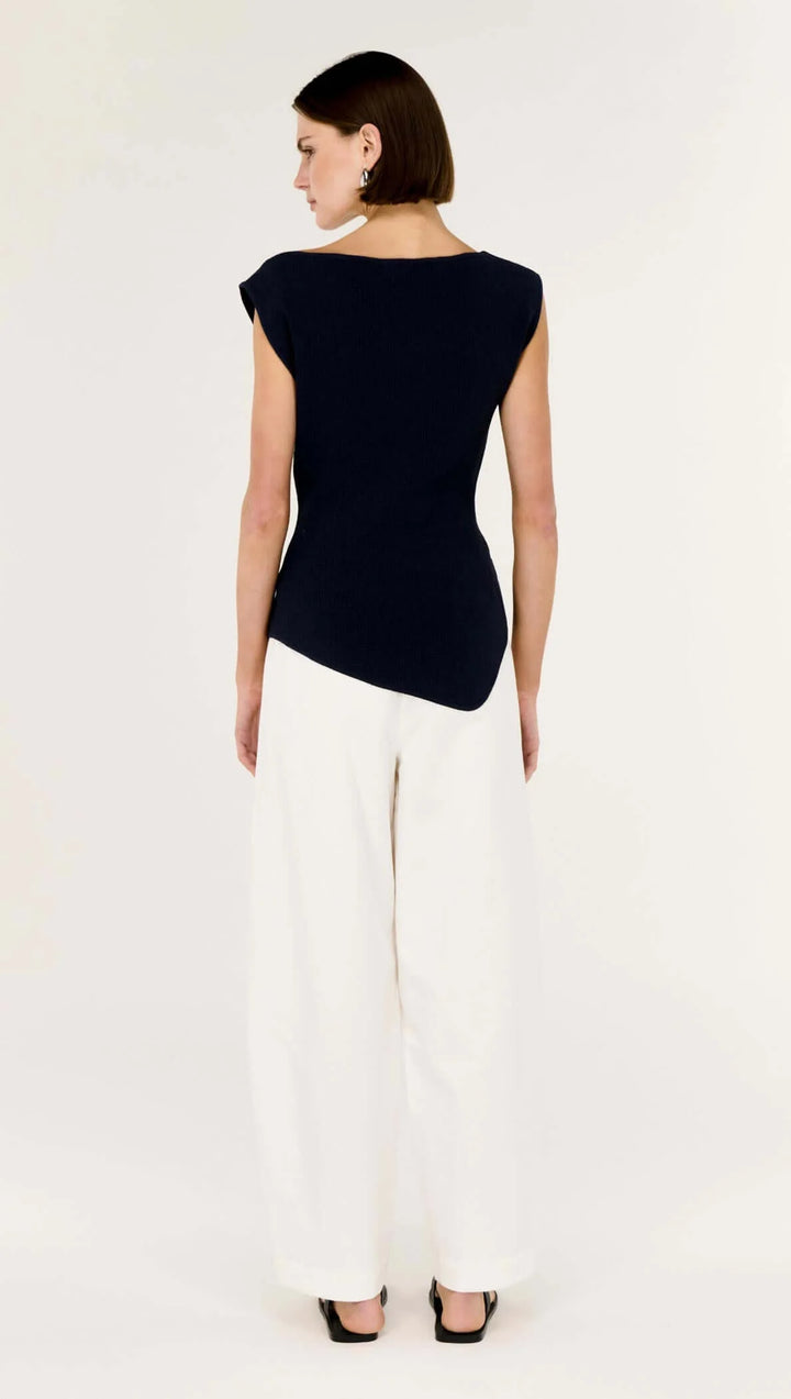 Woman wearing a black sleeveless top and white pants on a white background