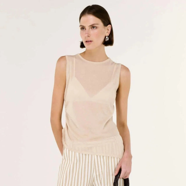 Woman wearing a beige sleeveless top and wide-leg pants, holding a black handbag on a white background