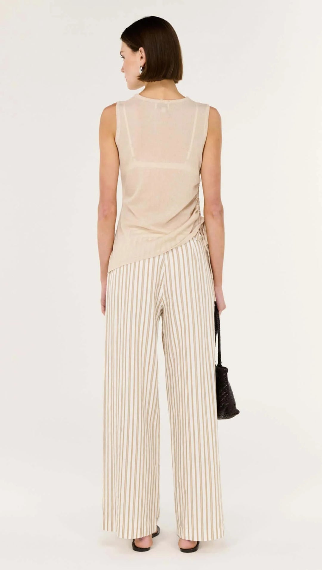 Woman wearing a beige sleeveless top and striped pants on a white background