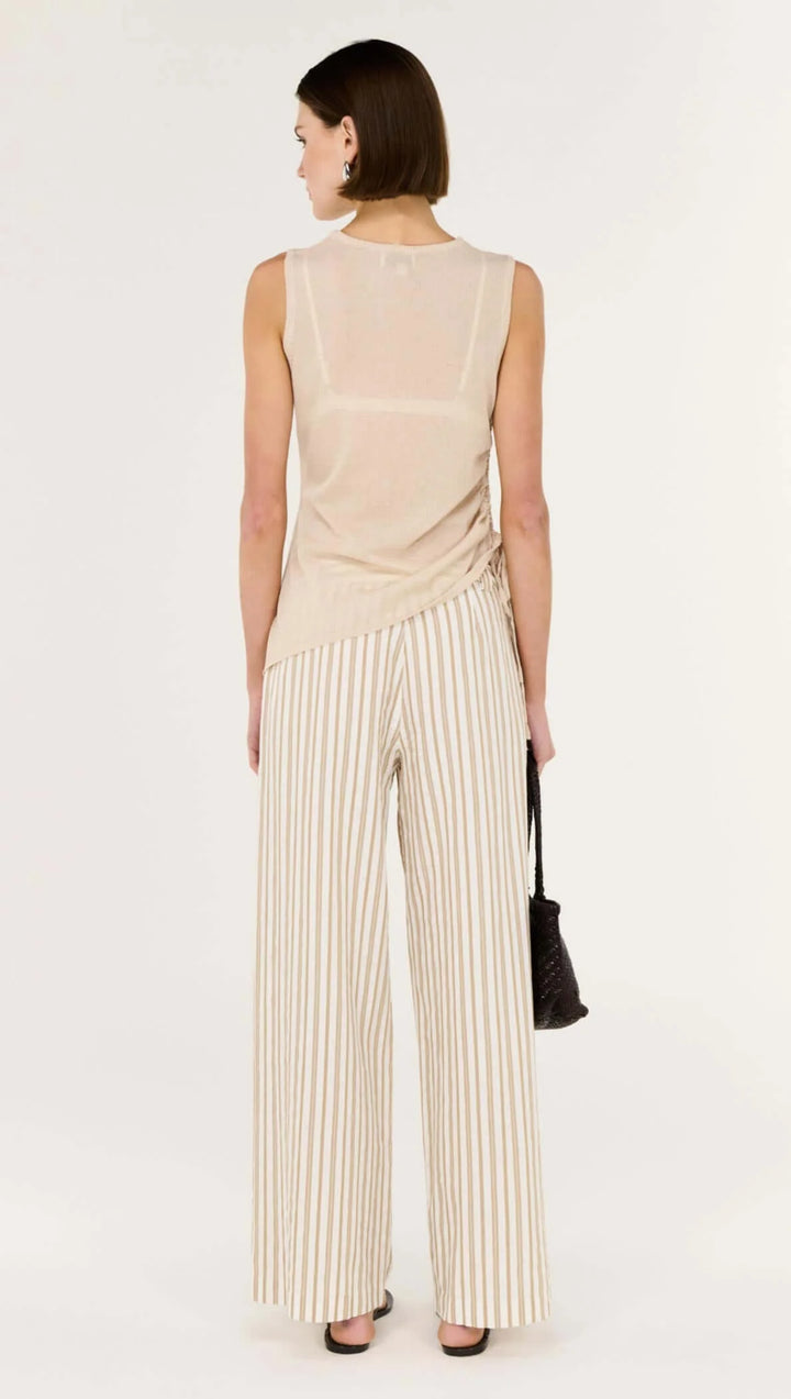 Woman wearing a beige sleeveless top and striped pants on a white background