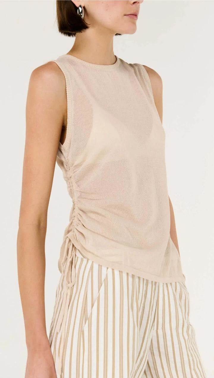 Woman wearing a beige sleeveless top and striped pants on a white background