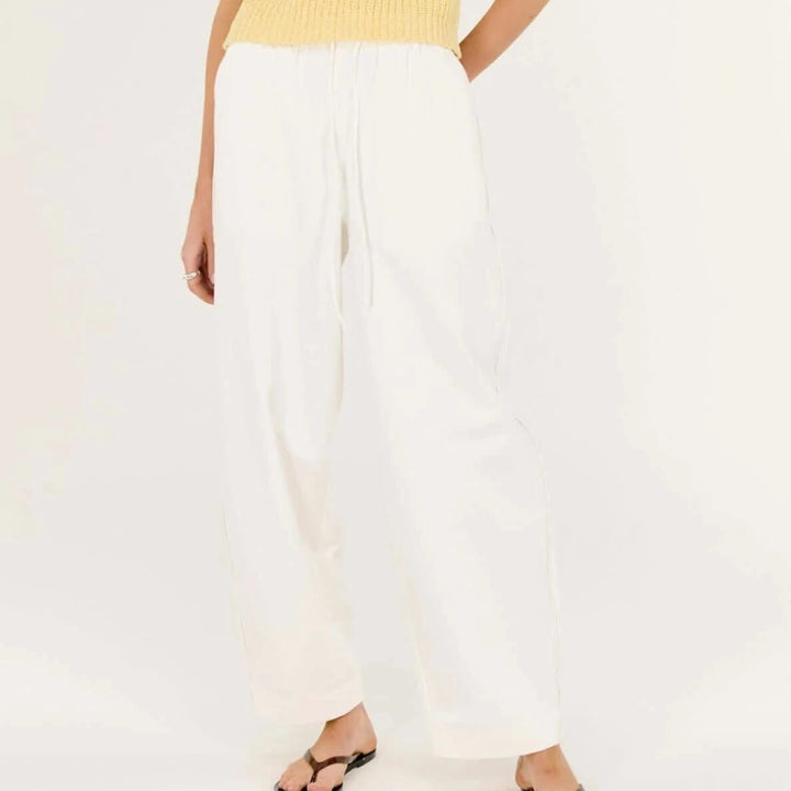 Woman wearing a yellow sleeveless top and white pants on a white background