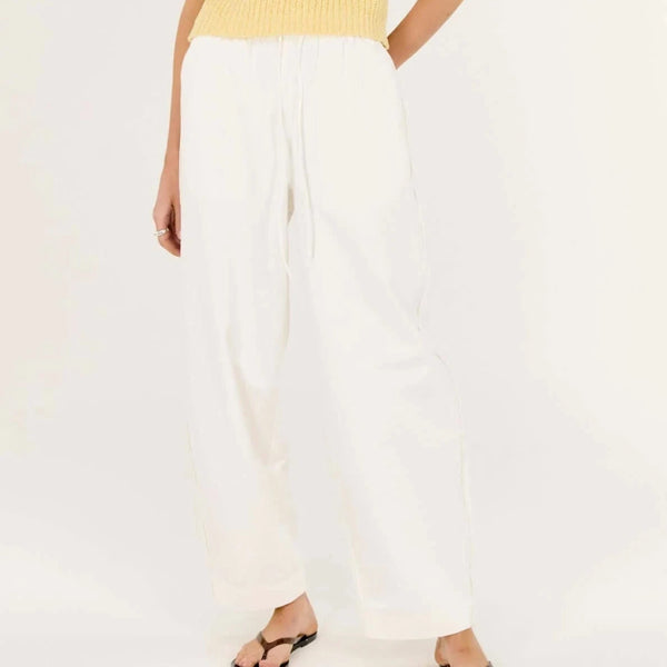 Woman wearing a yellow sleeveless top and white pants on a white background