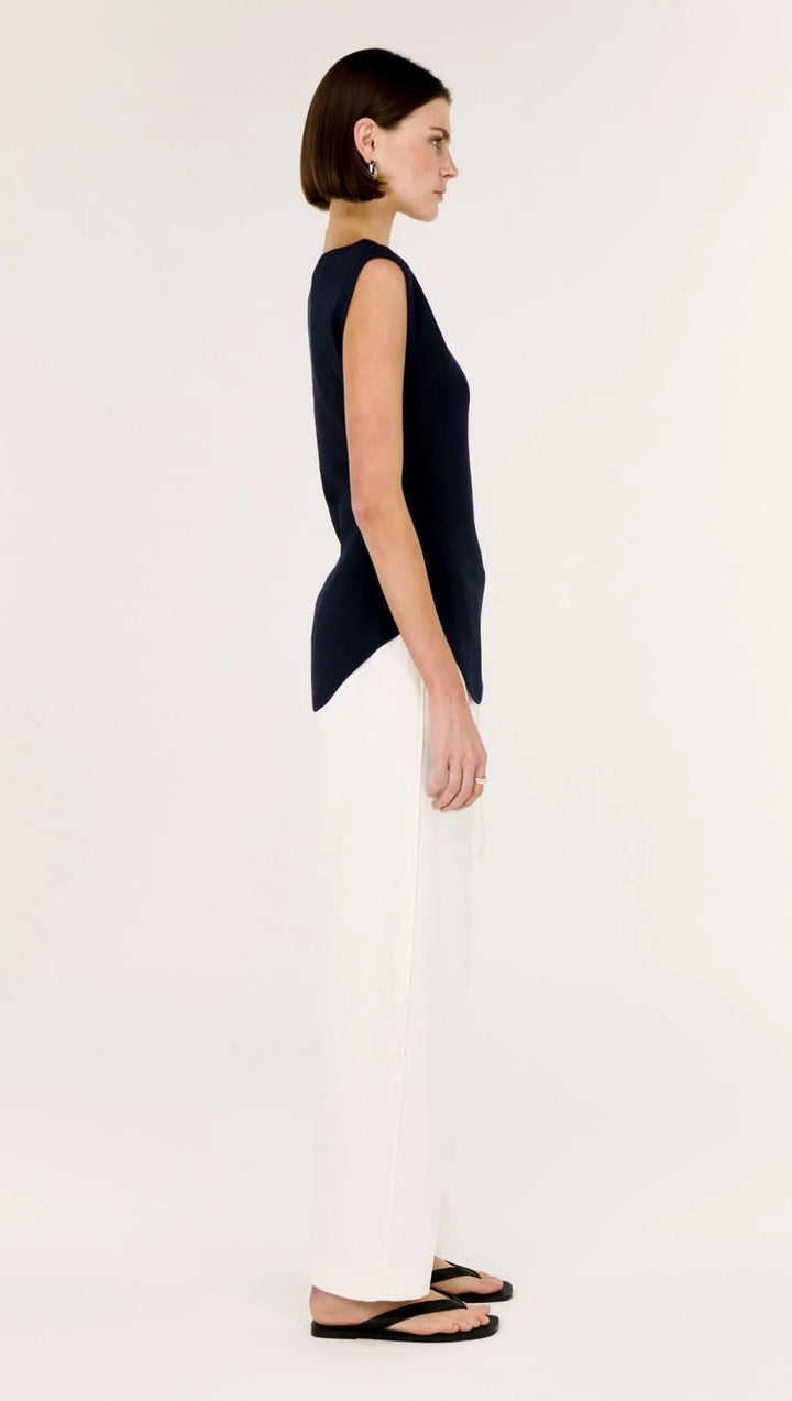 Woman wearing a navy sleeveless top and white pants on a white background