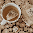 Tea cup with a tea bag on wooden logs, featuring a Better Tea brand bag.