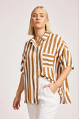 Woman wearing a eb & ive brown and white striped shirt with white pants on a light background