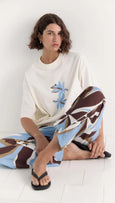 Woman sitting on the floor with a patterned blanket draped over her, wearing a white sweater with blue floral design.