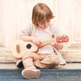 Child playing a ukulele with a wooden fence in the background