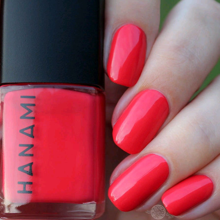 Red nail polish bottle with a hand displaying red nails against a green background