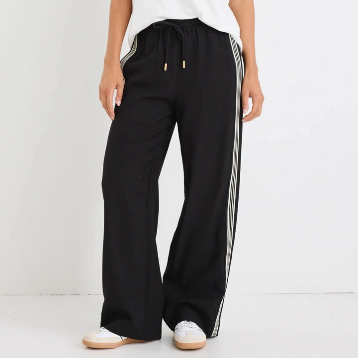 Woman wearing a white t-shirt and black vibe pants with side stripes on a white background