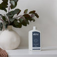 White bottle of 'alive' hand and body wash on a shelf with a vase and plant in the background