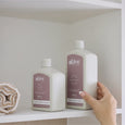 Two bottles of 'alive' hand and body products on a shelf with a hand reaching for one.