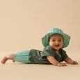 Baby wearing a green and white striped hat and outfit on a beige background