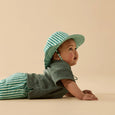 Baby wearing a green and white striped hat and outfit on a beige background