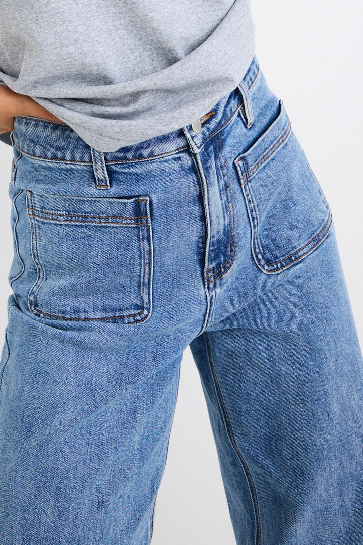 Close-up of blue Zoey  jeans with a gray shirt on a white background