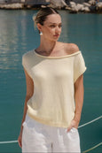 Woman wearing a light yellow top and white pants by a body of water.