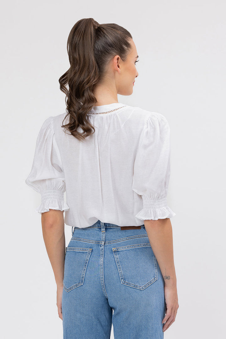 Woman wearing a white addyson blouse and blue jeans on a plain background