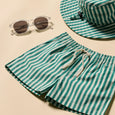 Green and white striped shorts with a matching hat and sunglasses on a beige background