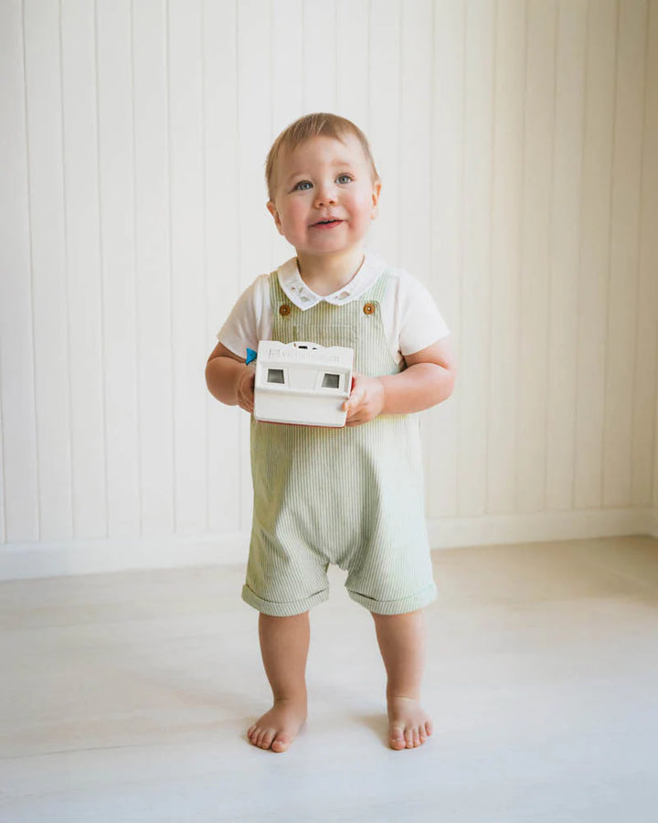Child holding a toy in a minimalistic room with white walls and floor.