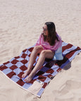 Woman sitting on a checkered towel at the beach