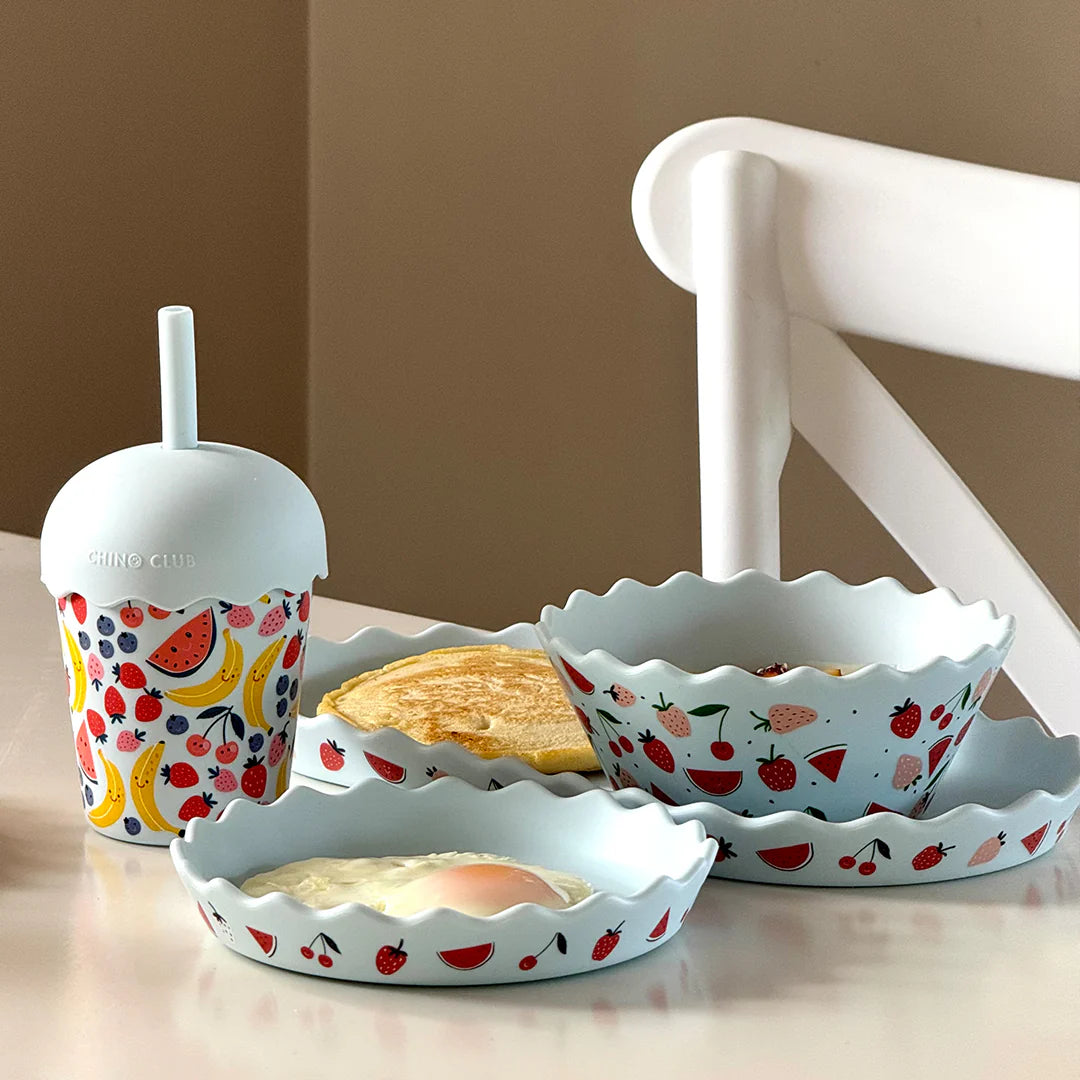 Set of ceramic dishes with fruit patterns on a table.