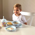 Child sitting at a table with a breakfast setup including bowls and a cup.