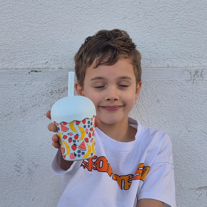 Child holding a colorful cup with a straw against a light gray wall