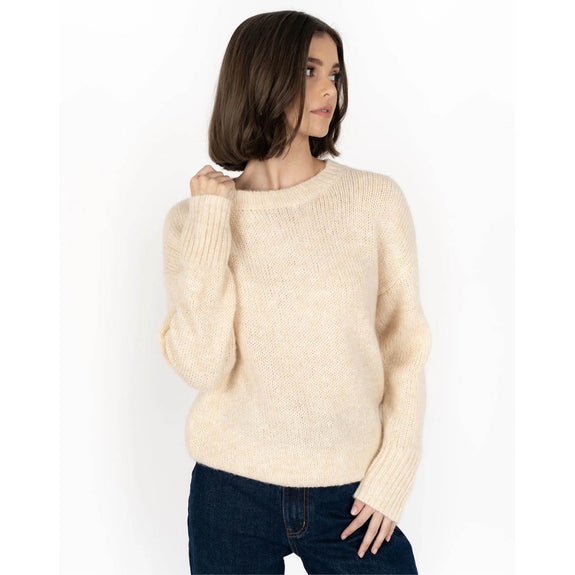 Woman wearing a beige sweater and dark jeans on a white background