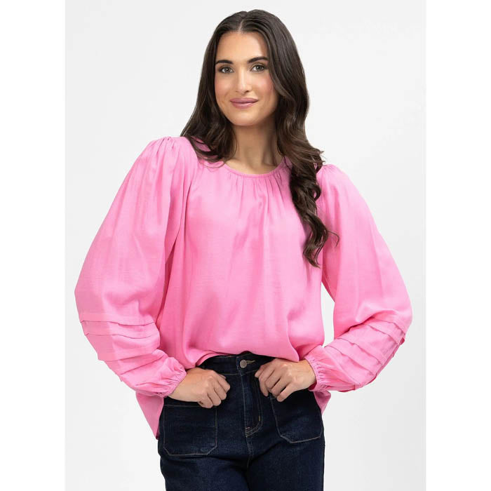 Woman wearing a pink Milly blouse and dark jeans on a white background