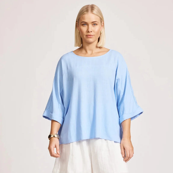 Woman wearing a light blue eb & ive top and white skirt on a plain background