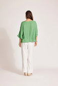 Woman wearing a eb & ive green top and white pants on a plain background