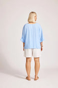 Person wearing a light blue eb and ive  top and white shorts on a plain background