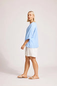 Woman wearing a light blue Eb & Ive top and white shorts on a plain background